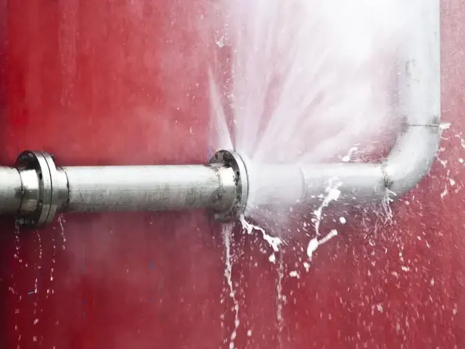 Water spraying from a failed supply pipe inside an opened wall